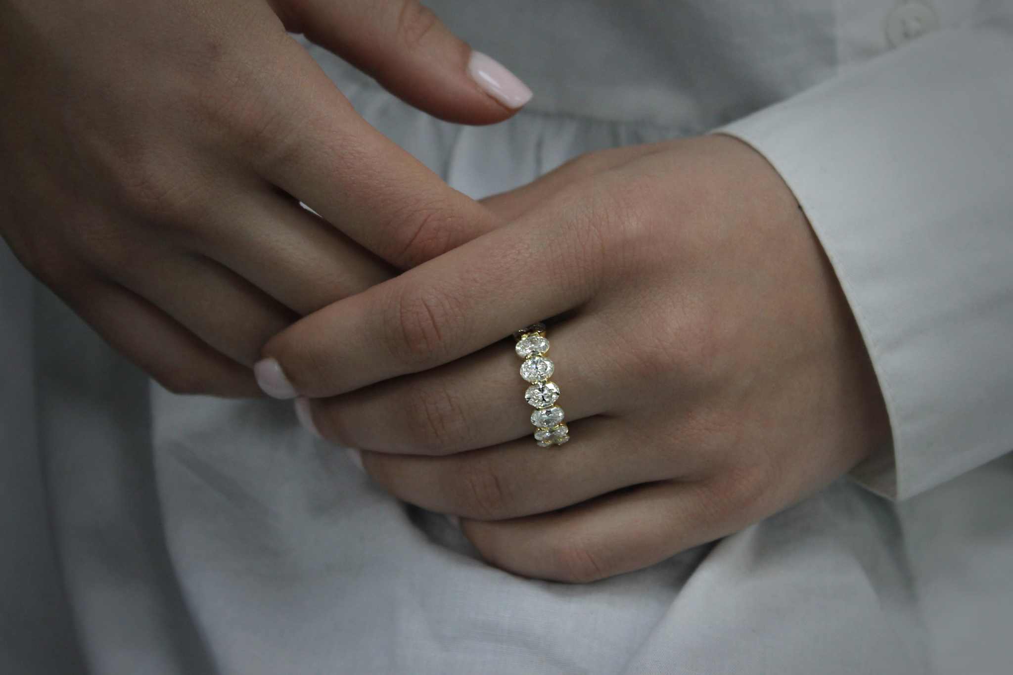Close-up of hand wearing Olivia Seven Stone Anniversary Band with oval cut diamonds in 18k yellow gold, showcasing elegant stone anniversary band design