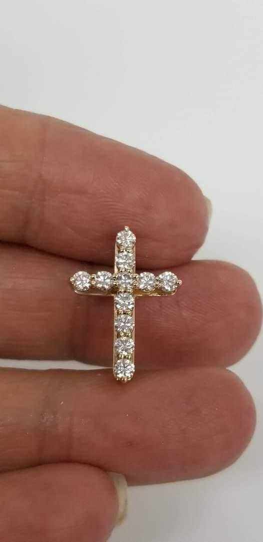 Close-up of a handcrafted 18k gold diamond cross pendant with sparkling F VS1 diamonds held between fingers.
